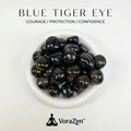 VoraZen™ Natural Blue Tiger's Eye Tumbled Stones in a white porcelain bowl. These deep midnight-blue crystals feature a silky chatoyant shimmer, known as the "Stone of Calm and Focus." High-quality polished finish, perfect for soothing anxiety and enhancing intuition.