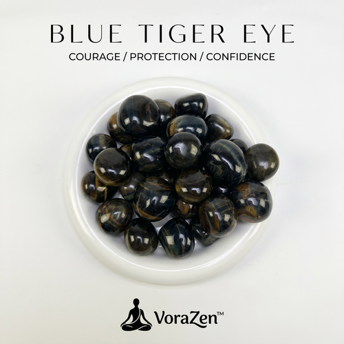 VoraZen™ Natural Blue Tiger's Eye Tumbled Stones in a white porcelain bowl. These deep midnight-blue crystals feature a silky chatoyant shimmer, known as the "Stone of Calm and Focus." High-quality polished finish, perfect for soothing anxiety and enhancing intuition.