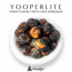 VoraZen™ Glowing Yooperlite Tumbled Stones in a white bowl. These unique Syenite stones contain fluorescent Sodalite that glows like fiery lava under UV light. Natural grey stones by day, glowing orange embers by night. High-quality polished finish for crystal collectors.